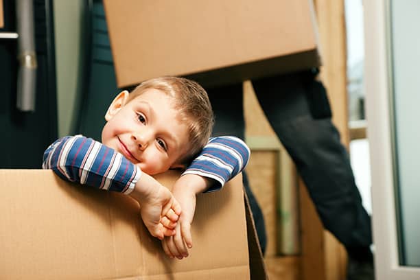 Pieni poika hymyilee istuen muuttolaatikossa