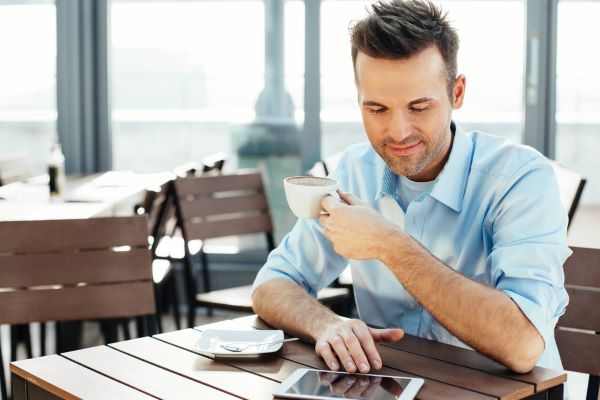 Tyytyväinen mies kahvilla tablet-tietokoneen kanssa.